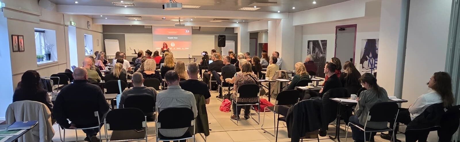 The full training room seen from the back, every seat taken, Ronia Fraser presenting at the front